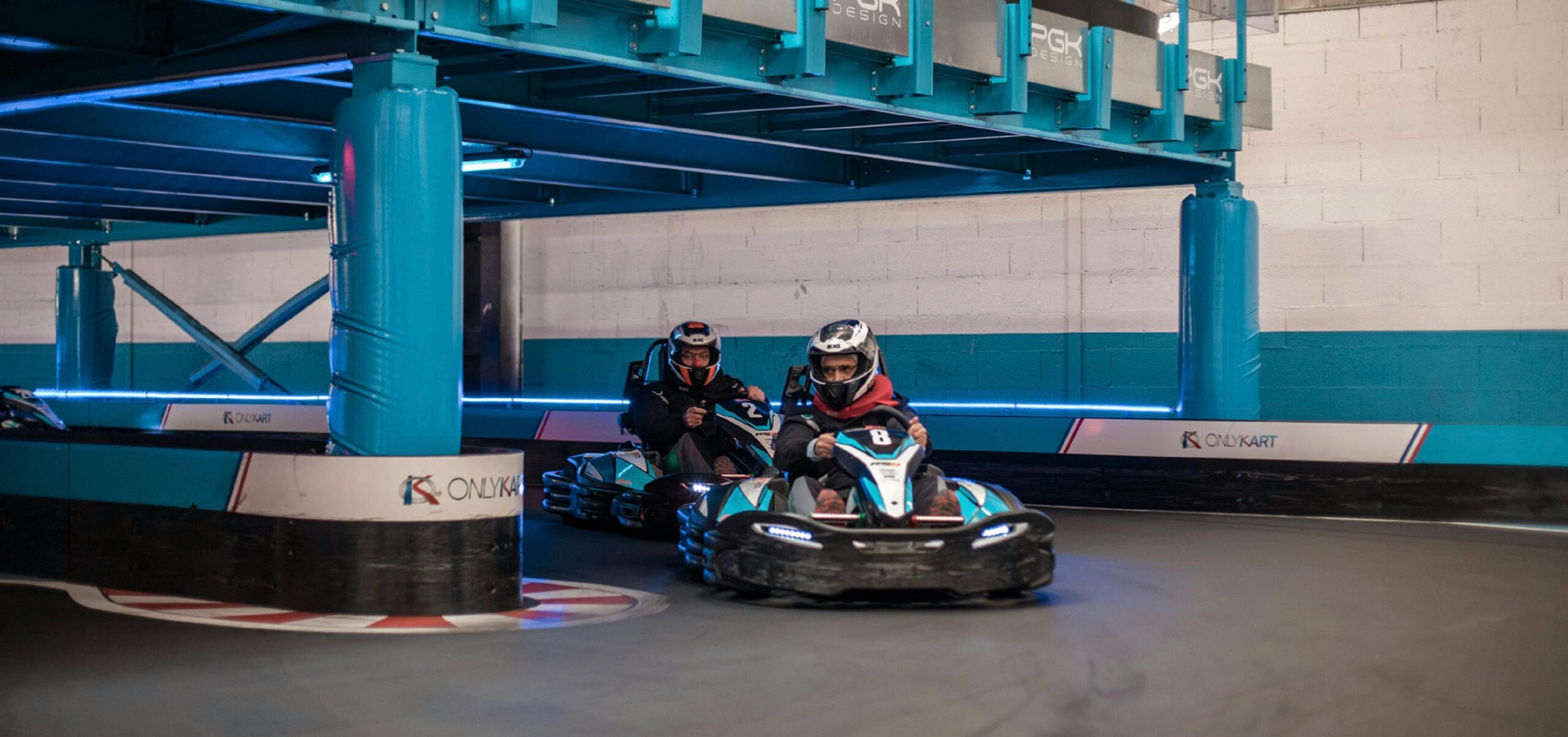 Intense indoor go-kart racing competition with racers maneuvering a sharp turn on the track.