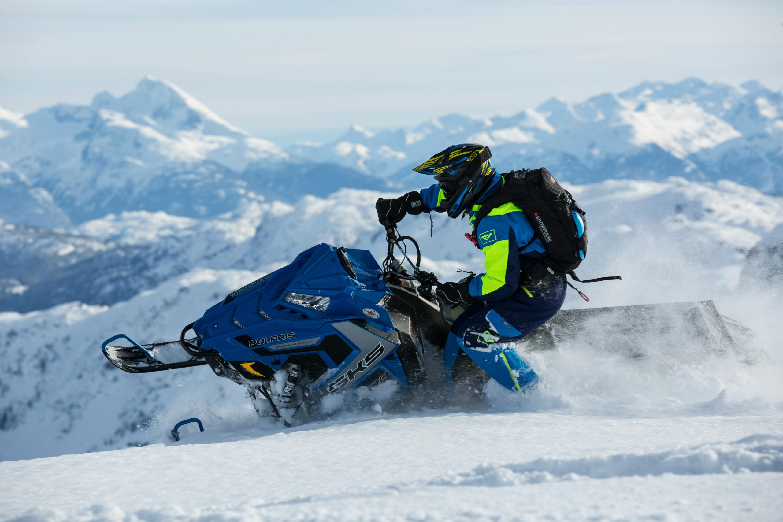 Man riding a snowmobile on snowy mountain, showcasing extreme winter sports adventure.
