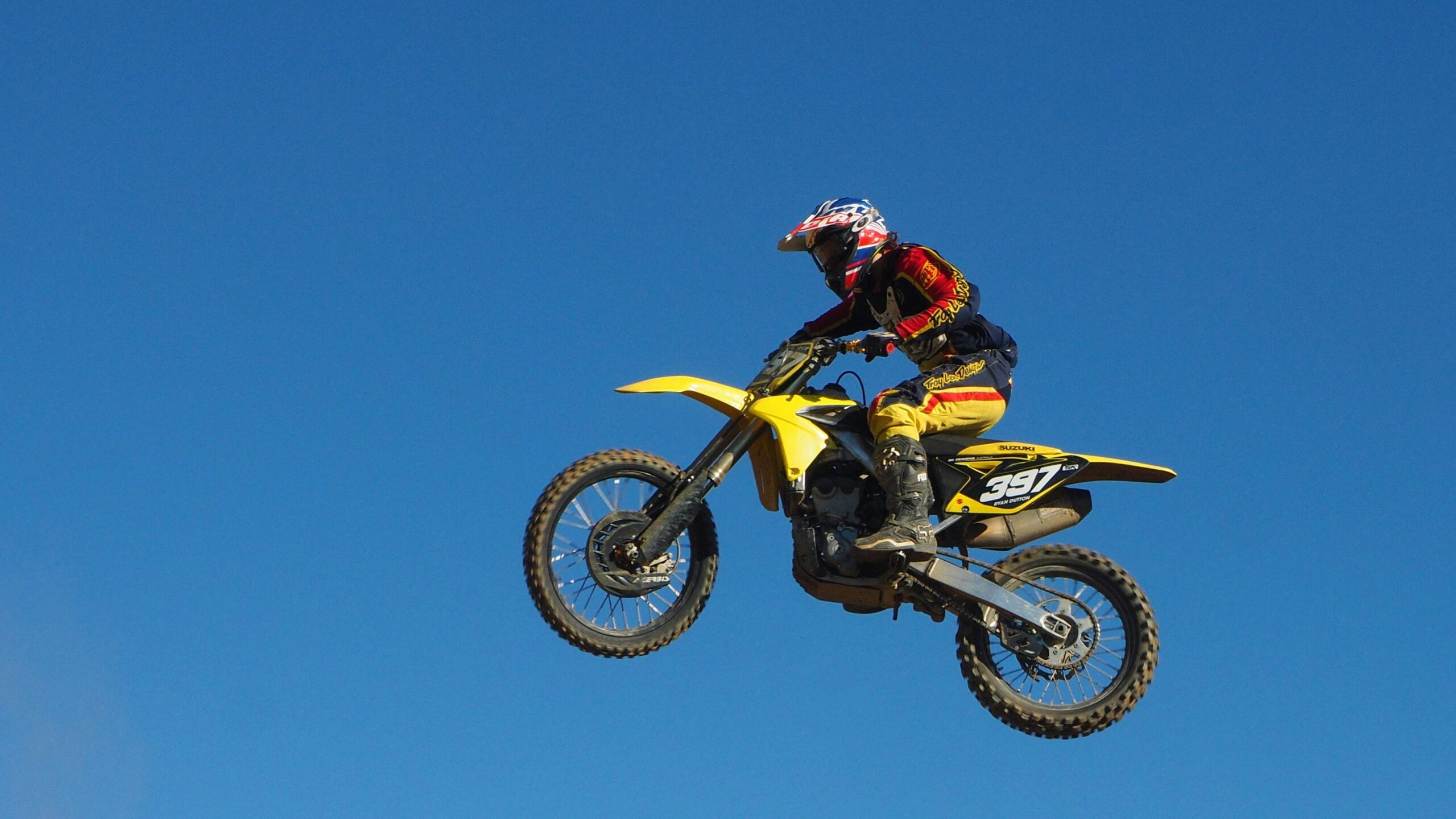 A motocross rider performs a daring jump on a yellow motorbike under a clear blue sky.