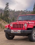 Red Jeep parked on dirt road with mountainous forest backdrop, ideal for travel and adventure themes.