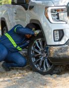Mechanic working on the wheel of a white off-road vehicle outdoors, fixing a problem.