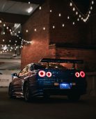 Rear view of a blue Nissan Skyline sports car on city streets at night, under string lights.