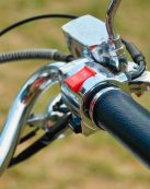 A detailed view of a bicycle handlebar featuring a red switch against a green blurred background.