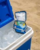 A blue cooler filled with ice sits open on a sandy beach, showcasing a sunny picnic vibe.