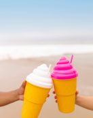 Refreshing summer drinks in beach setting with colorful lids and straws, captured against a blurred ocean backdrop.