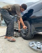 A young mechanic uses a lug wrench to fix a car tire outdoors.