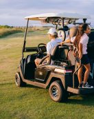 Family riding a golf cart on a sunny day at a scenic golf course.